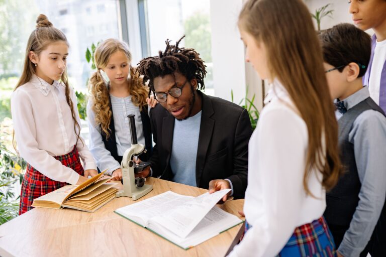 A secondary school teacher giving personalized instruction to a small group of students at his desk.
